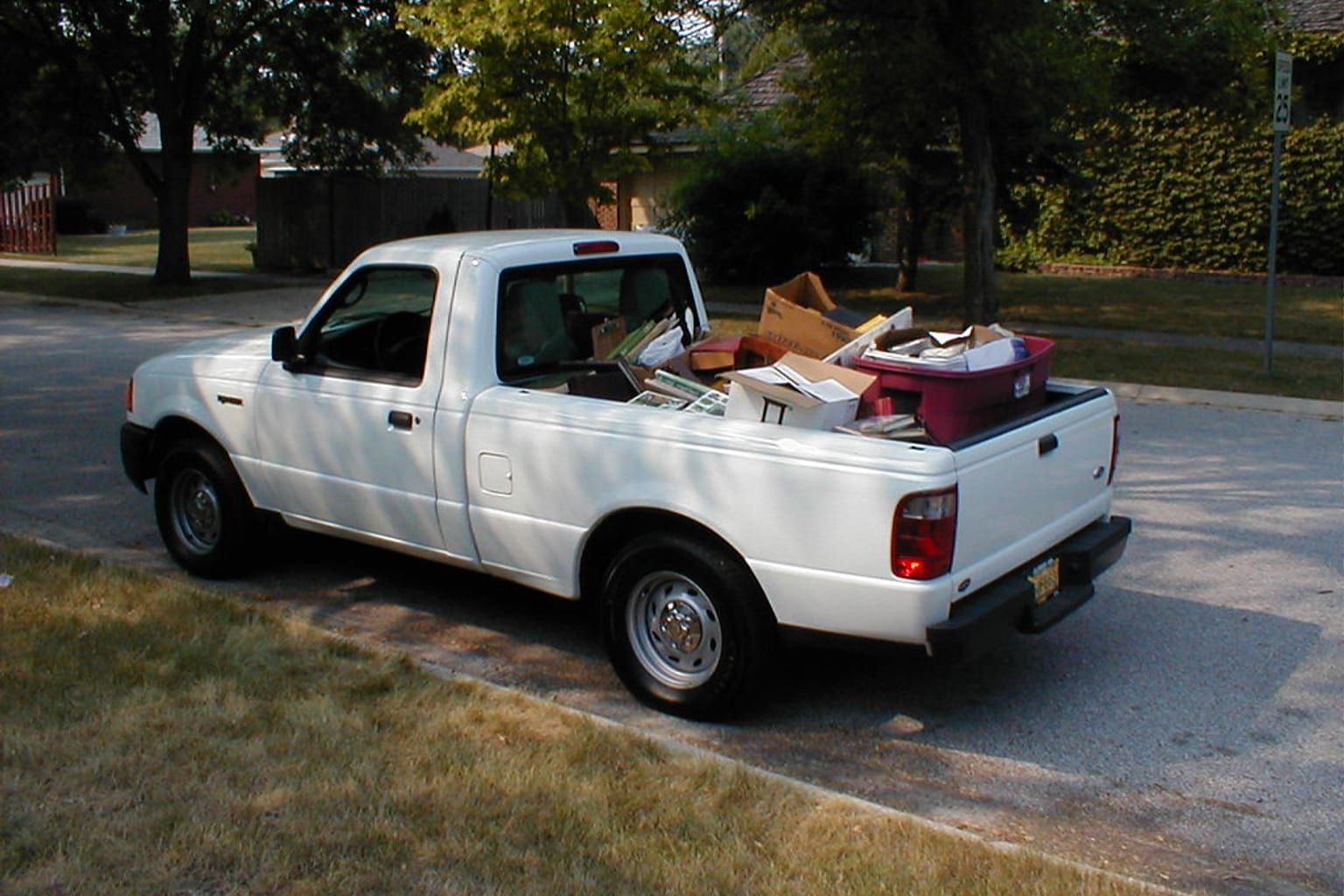 White pickup truck loaded with a mix of household junk and boxes on a residential street